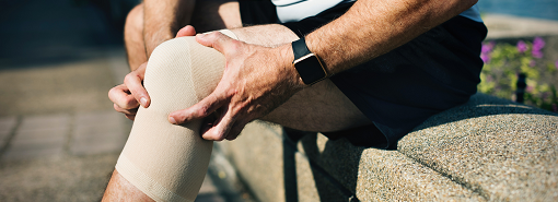 Man met een kniebandage om grijpend naar zijn knie