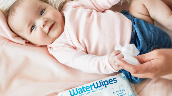 WaterWipes babydoekjes baby ligt op een roze deken en kijkt in de camera