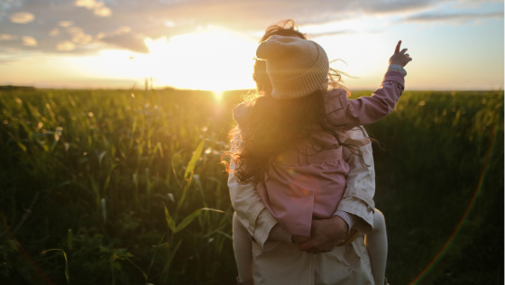 mama draagt dochter in een maisveld met zonsondergang