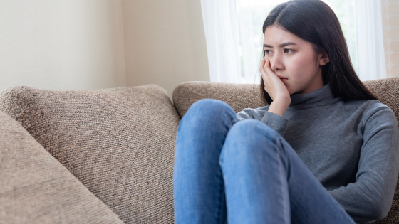 Een vrouw zit op de bank en maakt zich zorgen