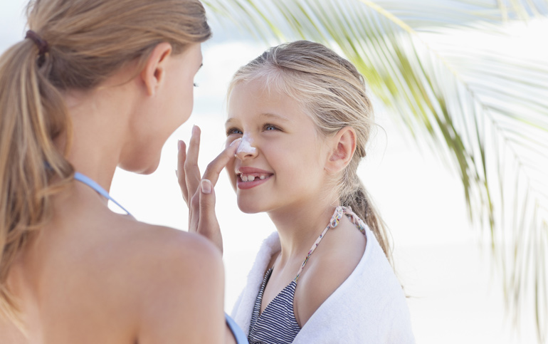 foto van een moeder die zonnebrandcrème op neus van haar dochter smeert