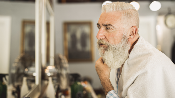 man met grijs haar en grijze baard kijkt bij kapper in de spiegel