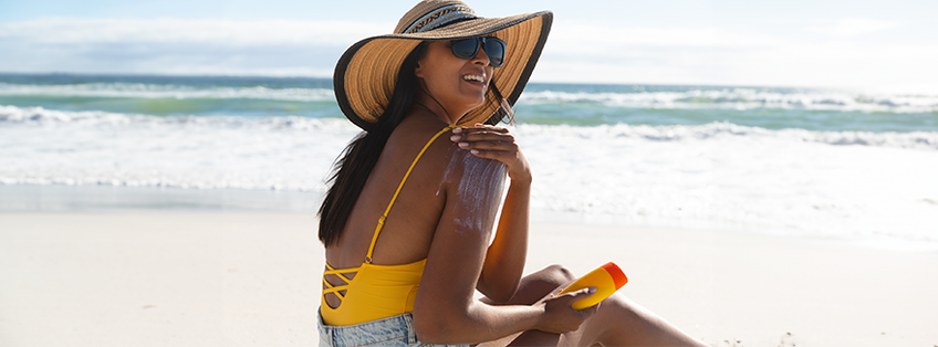 dame aan zee met zonnehoed smeert zich in met zonnebrand