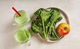 Bord met groene bladgroenten en een appel met ernaast twee glazen groene sap Bord met groene bladgroenten en een appel met ernaast twee glazen groene sap