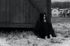 vrouw zit naast een schuur in zwarte kleding