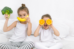 twee meisjes op bed met groente en fruit