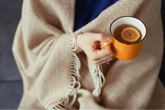 Vrouw zit onder een dekentje met thee